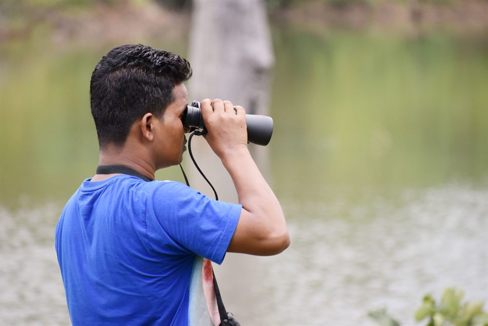 Man looking through binoculars beside a lake