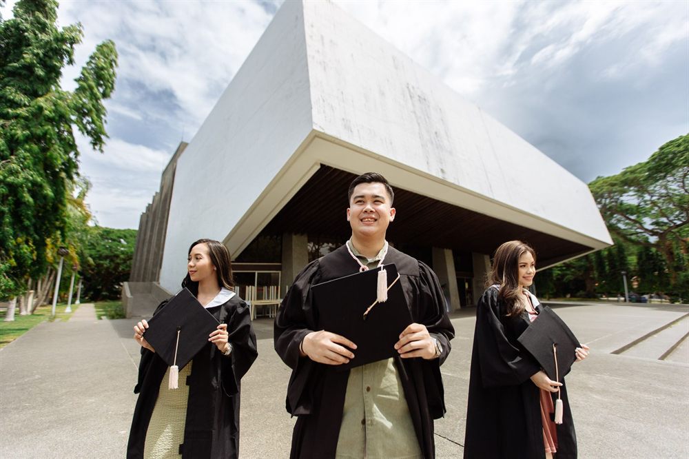 Three graduates in caps and gowns outside a modern campus building