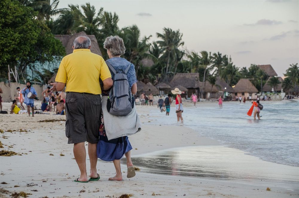 Older couple with backpacks walking along a tropical beach