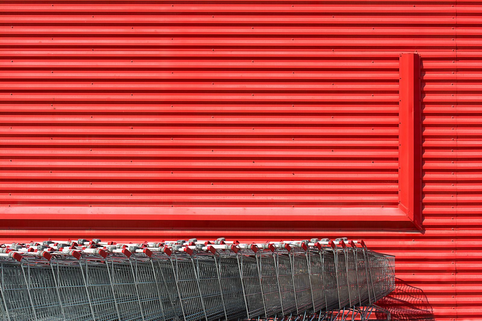 Row of shopping carts lined up against a red warehouse club wall